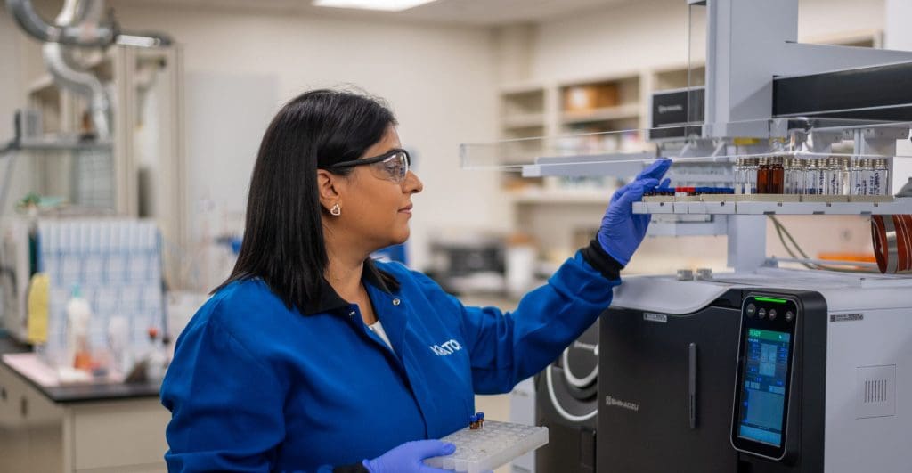 Innovation: A woman in a blue lab coat, wearing PPE conducts innovative chemistry research.
